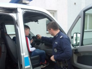 Policjant tłumaczy dziecku siedzącemu w radiowozie Fiat Ducato jak posługiwać się radiostacją.