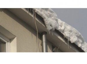 Fotografia przedstawia śnieg zwisający z gzymsu dachu bloku