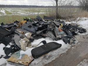 Fotografia przedstawia śmieci porzucone przy gruntowej drodze, widoczne elementy wyposażenia pojazdu - fotele, tapicerka itp.