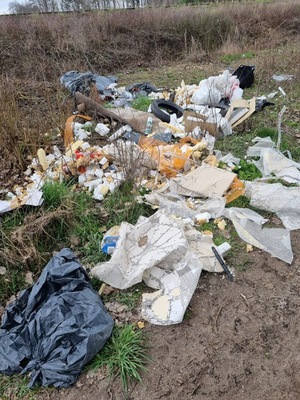 Fotografia przedstawia śmieci porzucone przy gruntowej drodze, dużo folii
