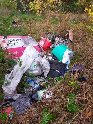 Fotografia przedstawia śmieci porzucone przy gruntowej drodze, worki z odpadami