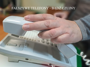 widok urządzenia - telefonu stacjonarnego ze słuchawką, nad nim ręka starszej osoby i napis fałszywe telefony - bądź czujny