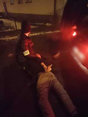 policjant nieumundurowany z zatrzymanym, który został obezwładniony i skuty. leży na podłożu obok pojazdu, policjant go przytrzymuje