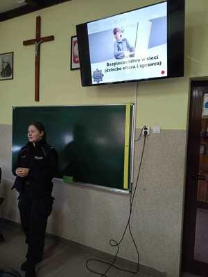policjantka stoi przy tablicy, powyżej na monitorze wyświetlana jest prezentacja