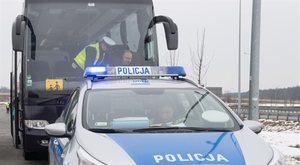 policjanci podczas kontroli autobusu, prze czarnym autokarem stoi radiowóz na sygnale