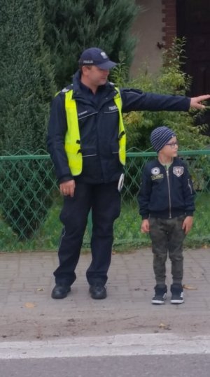 Policjant z dzieckiem, które demonstruje, w jaki sposób prawidłowo przejść przez jezdnię