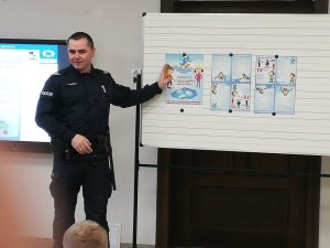 policjant omawiający temat zajęć pokazuje przedstawione na plakacie zagrożenia podczas zabawy na lodzie