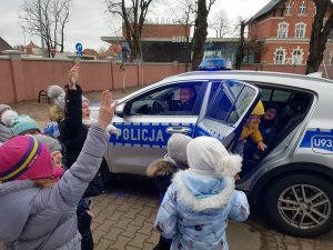Policjant prezentuje radiowóz, dzieci go oglądają. Policjant siedzi za kierownicą.