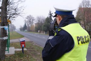 policjant stoi przy drodze i mierzy prędkość
