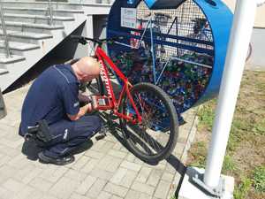 Policjant wykonuje grawer na ramie roweru przed komendą policji