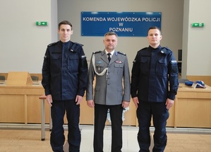 Dwóch policjantów z komendantem Powiatowym Policji stoją do zdjęcia, w tle baner KWP w Poznaniu