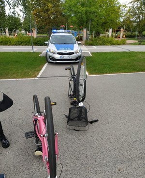 dwa rowery na drodze asfaltowej, w oddali stoi radiowóz