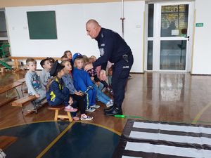 Policjant opowiada dzieciom siedzącym na ławce o niebezpieczeństwach