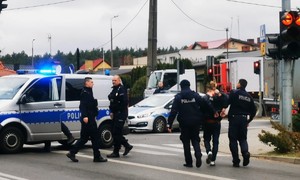 policjanci prowadzą zatrzymanego do radiowozu stojącego na ulicy