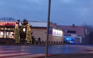 Policjanci stoją przed radiowozem koło drogi przy przejściu dla pieszych, obok dwie donice przybrane lampkami przypominaja choinki