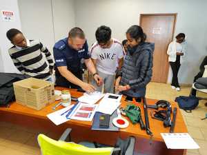 policjant podczas czynności zdejmowania odcisków palców osoby - kolejna fotografia, na stole widać wyposażenie do służby policjanta