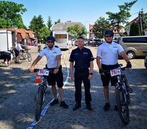 trzech policjantów stoją naprzeciwko fotografa, jeden w granatowym umundurowaniu, dwóch w letnim z dwoma rowerami
