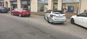 dwa samochody stoją zaparkowane na miejscu parkingowym przy jezdni, jeden z nich srebrna toyota ma widocznie uszkodzony tylny zderzak.
