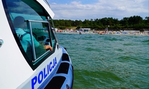 fotografia przedstawia patrol policji w motorówce na wodzie, w oddali plaża