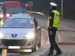 policjant podchodzący do auta z urządzeniem.