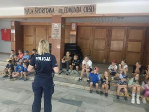 policjantka stoi przed dziećmi, które siedzą na schodach