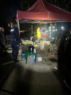 zdjęcie nocne, policjanci rozstawiają namiot, pod nim organizowana jest kuchnia polowa