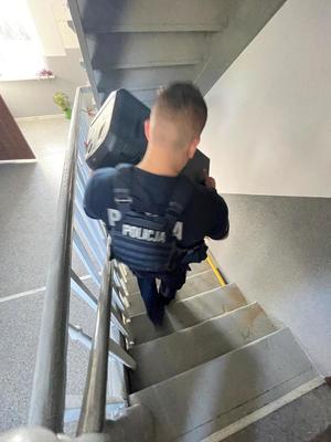 policjant pomaga znieść walizkę po schodach bloku