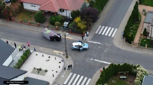 zdjęcie kolizji wykonane dronem z wysokości. Pojazd bus przewrócony na jezdni, obok stoi radiowóz i policjanci