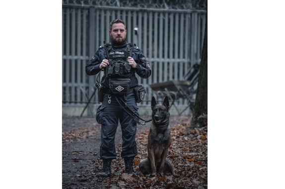 policjant stoi obok psa służbowego, w tle widać płot na granicy