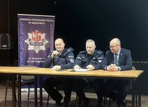 Dwóch policjantów i burmistrz siedzą przy stole prezydialnym