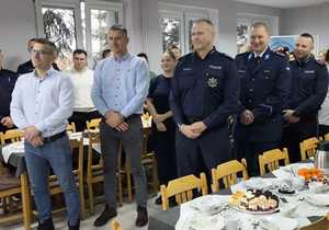 zdjęcie ogólne policjantów i pracowników na sali świetlicy stojących przy stole wigilijnym