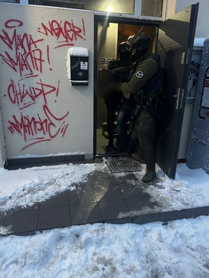 Policjanci wyprowadzaja zatrzymanego z klatki schodowej, na której jest m.in. graffiti HWDP