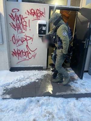 Policjanci wyprowadzaja zatrzymanego z klatki schodowej, na której jest m.in. graffiti HWDP - kolejne ujecie