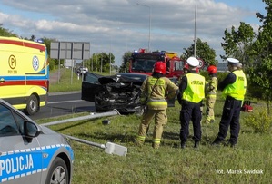 policjanci i strażacy stoją na poboczu przy rozbitym na latarnii samochodzie