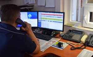 policjant dyżurny siedzący w miejscu pracy, trzymający w ręku słuchawkę telefonu