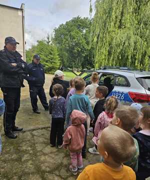 kolejne ujęcie policjanta z dziećmi przy radiowozie pokazującego wyposażenie służbowe