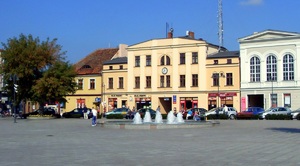 widok na rynek  widać fontanne i drzewo w oddali