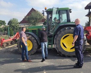 Policjant i rolnicy stoją przy ciągniku na jezdni