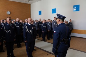 policjant składa meldunek komendantowi, w tle inne osoby
