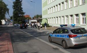 Radiowóz stoi koło wejścia do szkoły, obok przechodzą rodzice i dzieci