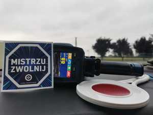 urządzenie miernik prędkości, lizak i naklejka mistrzu zwolnij leżą na podszybiu radiowozu