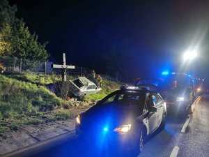 pojazd po zdarzeniu drogowym stoi na poboczu pod krzyżem przydrożnym, przed nim stoi radiowóz na sygnale