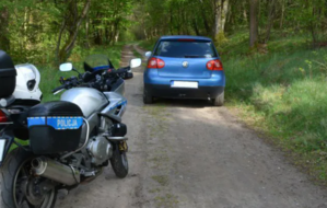 motocykl policyjny, przed nim samochód zaparkowany na drodze leśnej