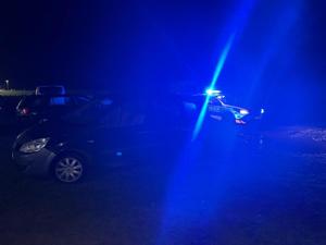 widok zatrzymanego pojazdu renault, za nim radiowóz na błyskach, wokół nic nie widać z uwagi na mrok