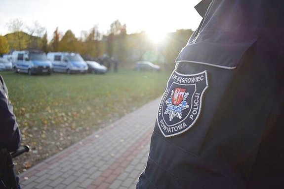 zdjęcie z naszywką policjanta na ramieniu KPP Wągrowiec, w tle widać radiowozy