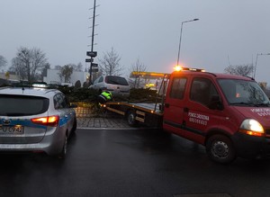 samochód na nasypie ronda, obok niego radiowóz i pojazd pomocy drogowej