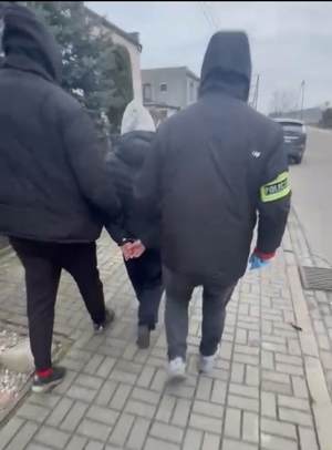 lichtarze i krzyże zabezpieczone przez policjantów, zatrzymany w bluzie, zatrzymany prowadzony przez policjantów na ulicy