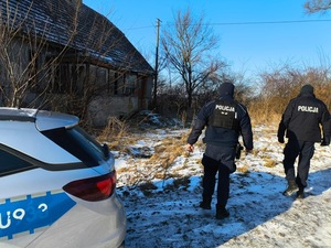 policjanci kontrolujący pustostany, przy radiowozie z kocami, w budynku