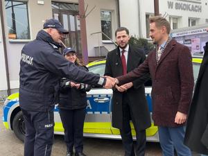 zdjęcia z uroczystości przekazania radiowozu, samochód stoi przed budynkiem rady miejskiej przy jezdni, przy samochodzie stoją osoby - burmistrzowie, komendanci i przewodniczący - 5 osób. radiowóz ma włączone sygnały świetlne