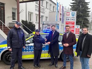 zdjęcia z uroczystości przekazania radiowozu, samochód stoi przed budynkiem rady miejskiej przy jezdni, przy samochodzie stoją osoby - burmistrzowie, komendanci i przewodniczący - 5 osób. radiowóz ma włączone sygnały świetlne